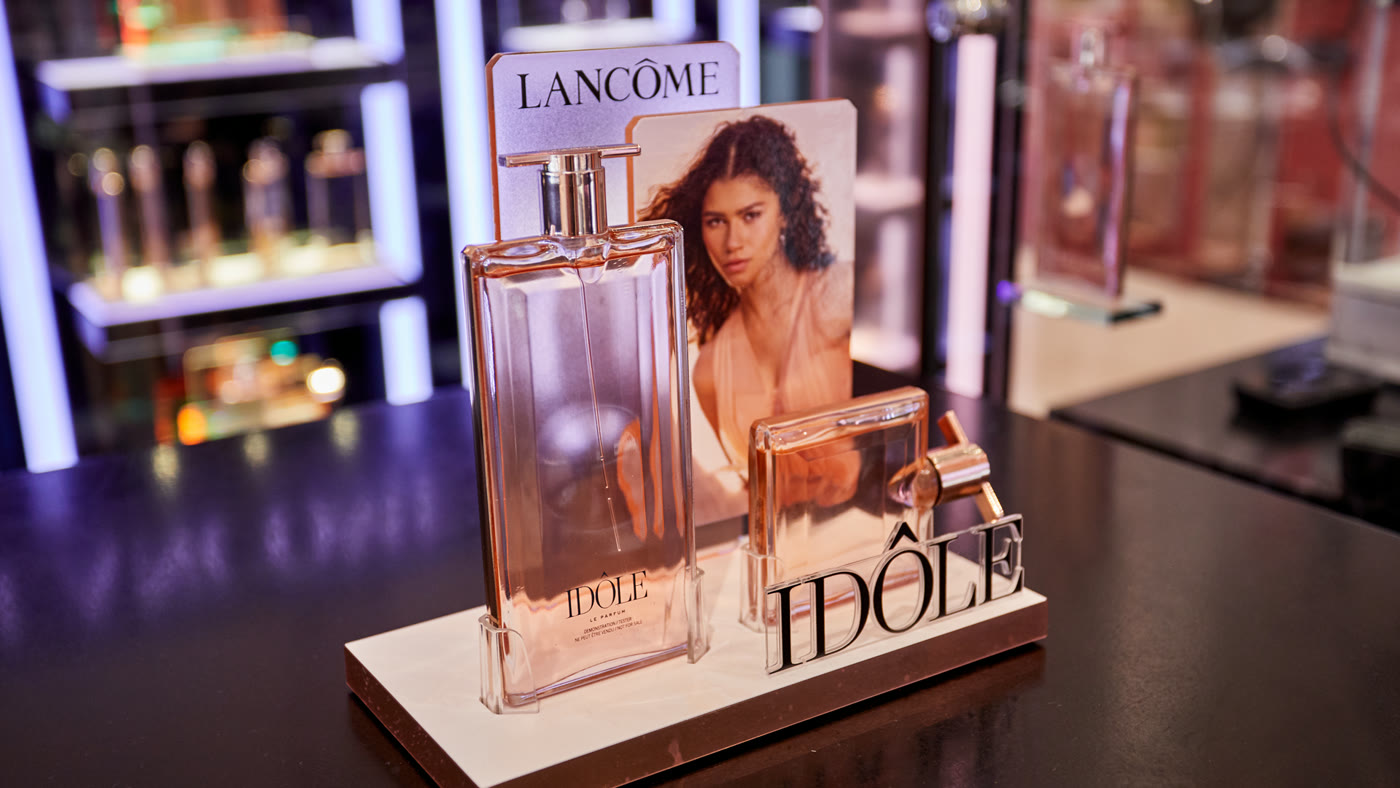 Idôle fragrance bottle on a counter display with campaign visual